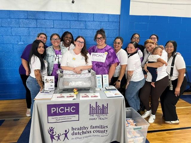 A group of people surrounding a table with logos from the Institute for Family Health, Healthy Families of Dutchess County and PICHC.